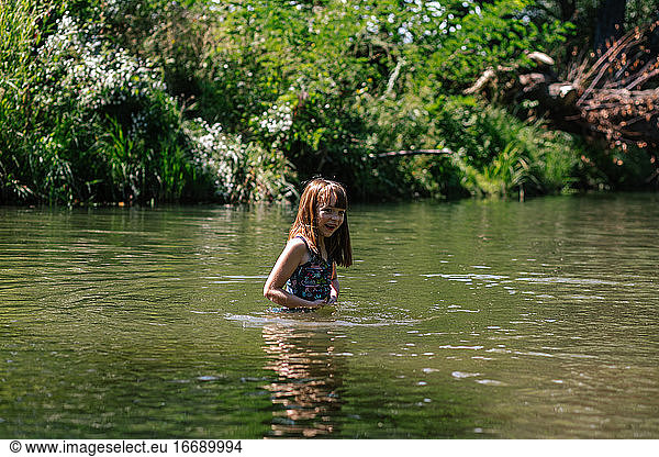 Happy young girl swimming in a deep creek on a summer day
