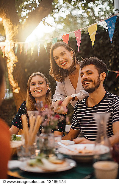 Happy young male and female friends at table during dinner party in backyard