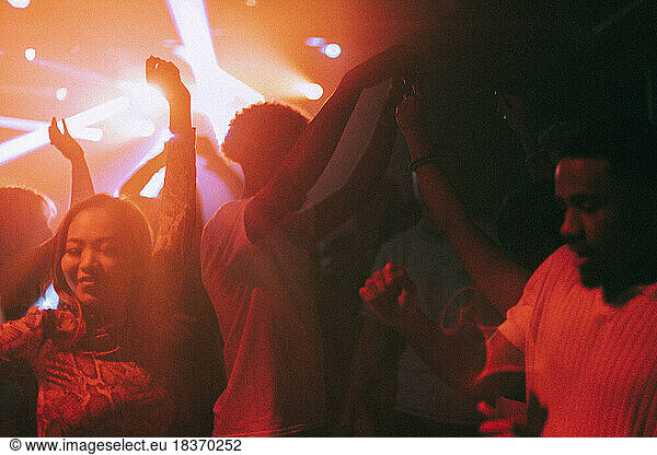 Happy young male and female friends enjoying dance at illuminated red nightclub