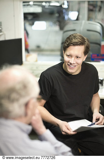 Happy young male mechanic discussing over document with customer in office