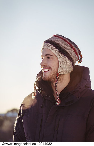 Happy young man looking away against clear sky during winter