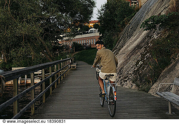 Happy young man looking over shoulder while cycling on pier