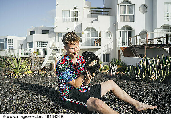Happy young man sitting with dog in front yard