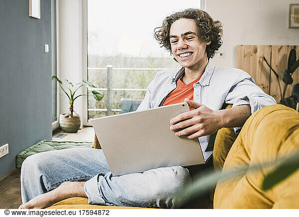 Happy young man using laptop sitting on sofa in living room