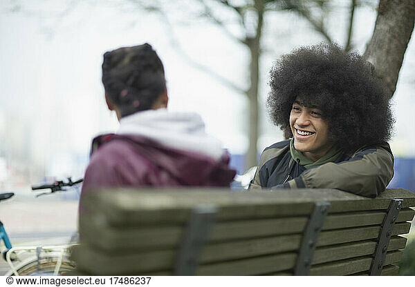Happy young man with afro talking to friend on park bench