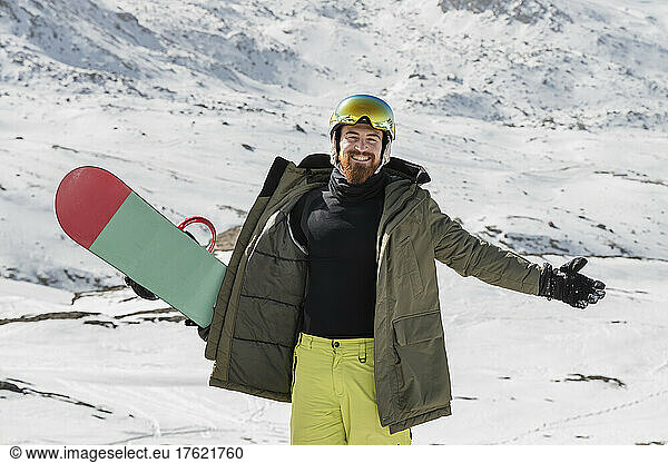 Happy young man with arms outstretched standing on snowcapped mountain