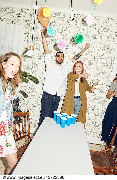 Happy young man with arms raised and female friends standing at dinner party