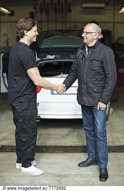 Happy young mechanic shaking hands with male customer at auto repair shop