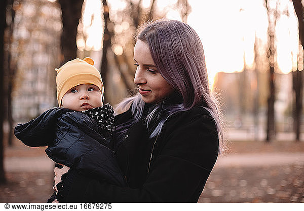 Happy young mother carrying baby son standing in park in autumn