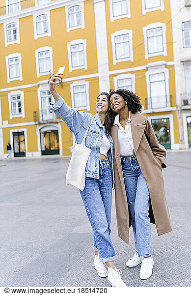 Happy young multiracial friends taking selfie in front of yellow building