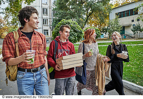 happy young people walking with pizza and drinks on the street