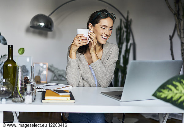 Happy young woman at home with laptop on desk
