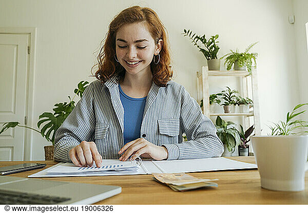 Happy young woman calculating financial graph at home