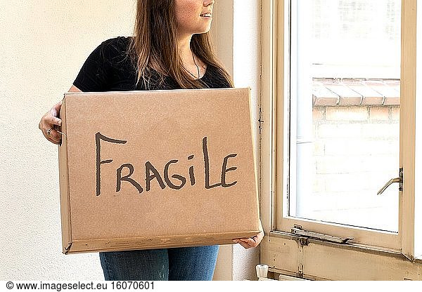 Happy young woman carrying a cardboard moving box for her new home  moving or new house concept fragile and retro.