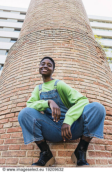 Happy young woman crouching in front of brick column