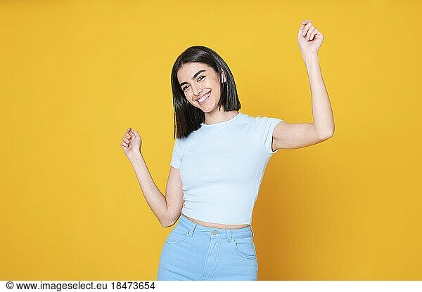 Happy young woman dancing against yellow background