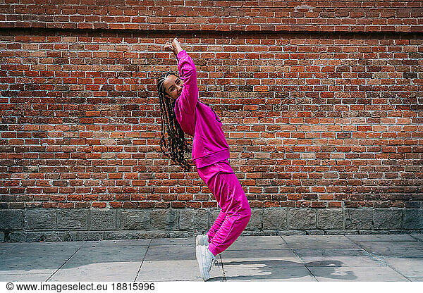 Happy young woman dancing in front of brick wall