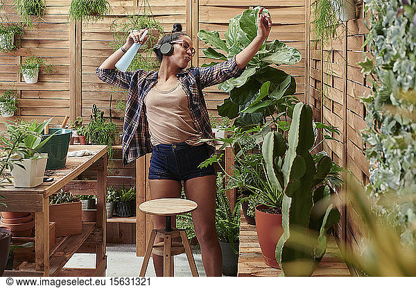 Happy young woman dancing on her terrace while gardening