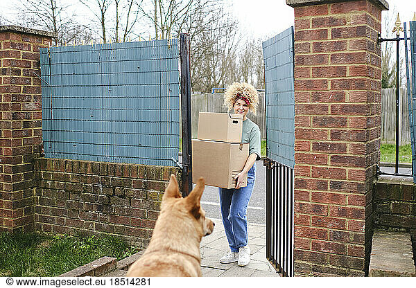 Happy young woman delivering packages entering through gate
