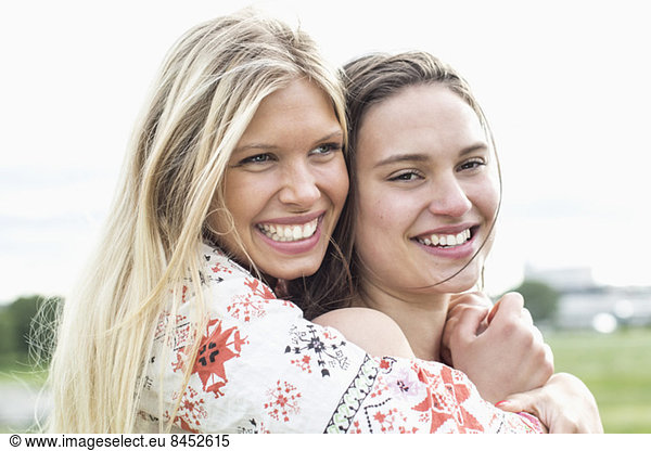 Happy young woman embracing female friend against clear sky