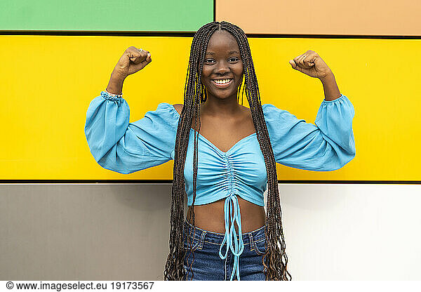Happy young woman flexing muscles in front of multi colored wall
