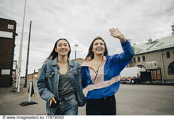 Happy young woman gesturing while walking with friend on street in city