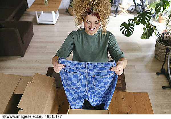 Happy young woman holding checked jeans at desk