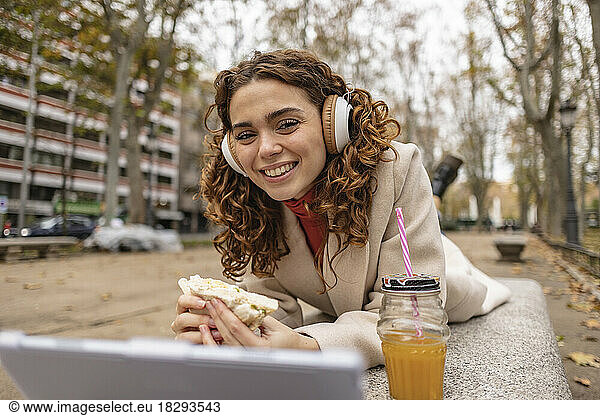 Happy young woman holding sandwich and lying on seat