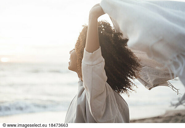 Happy young woman holding scarf at beach