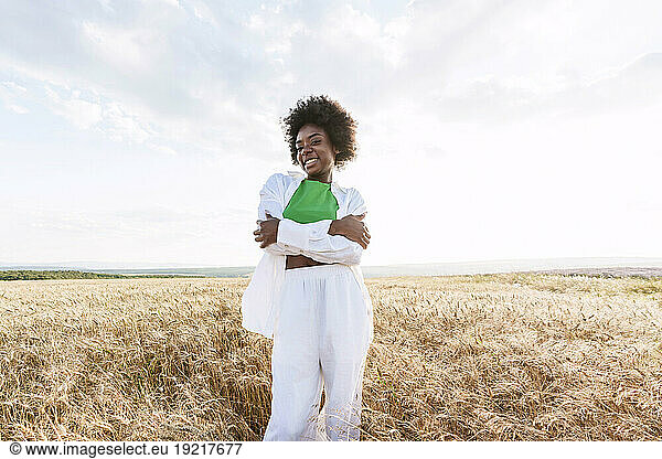 Happy young woman hugging self standing in field