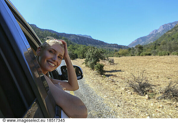 Happy young woman leaning on car window enjoying sunny day