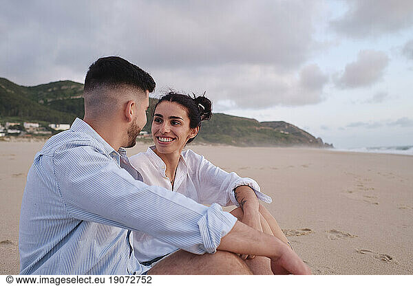 Happy young woman looking at boyfriend sitting at beach