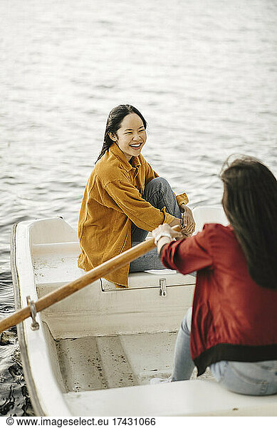 Happy young woman looking at female friend rowing boat