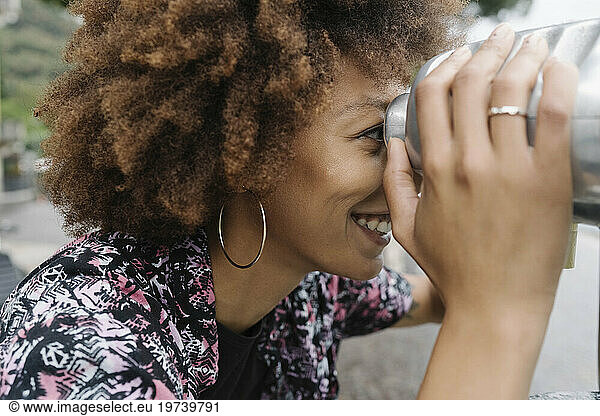 Happy young woman looking through coin operated binoculars