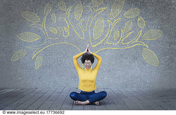 Happy young woman meditating under tree painted on wall