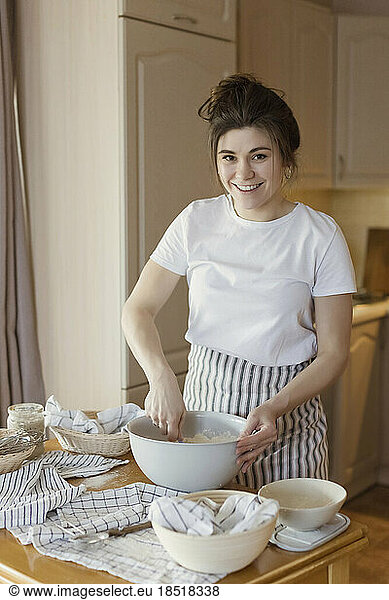Happy young woman mixing bread dough at home