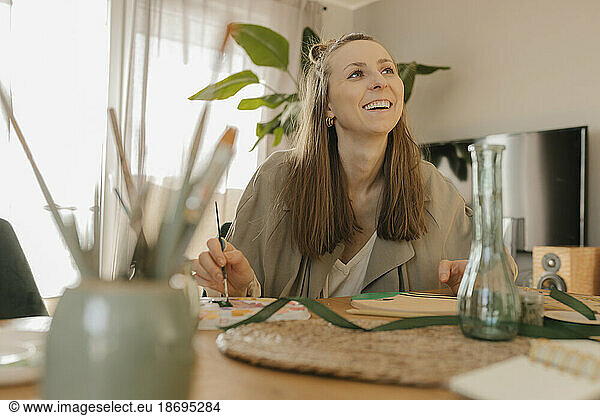 Happy young woman painting while sitting at table