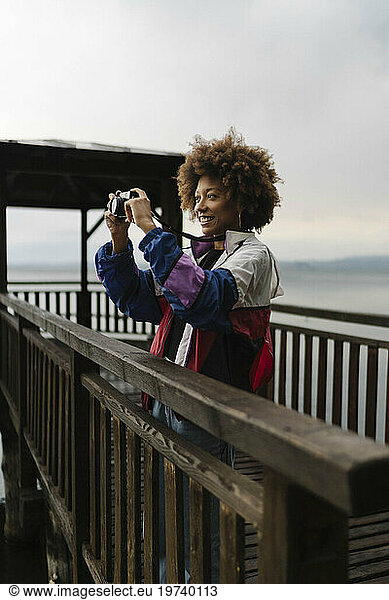 Happy young woman photographing through camera on footbridge