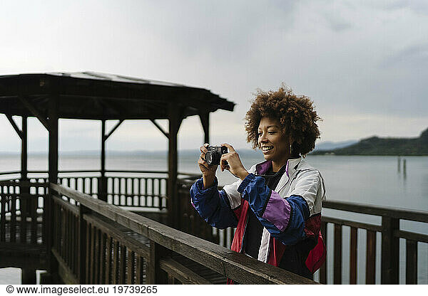 Happy young woman photographing with camera in front of lake