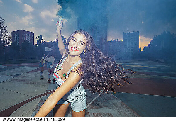 Happy young woman playing with smoke torch at sports court