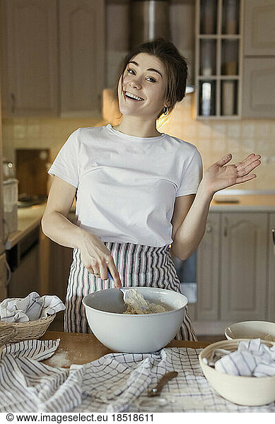 Happy young woman pointing at bread dough in bowl