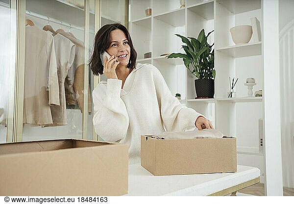 Happy young woman recycling clothes and talking on smart phone at home