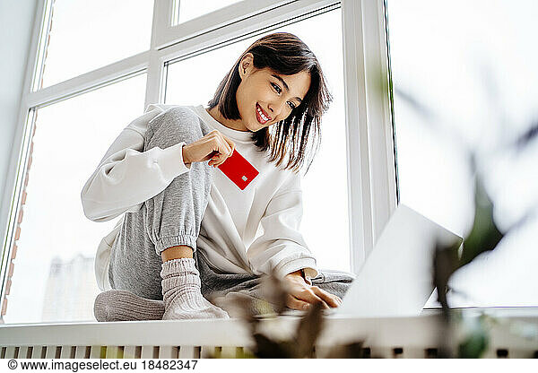 Happy young woman shopping with credit card on laptop at home