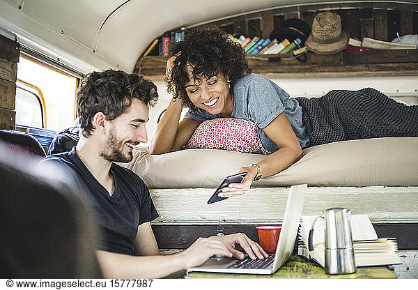 Happy young woman showing mobile phone to man sitting with laptop in motor home