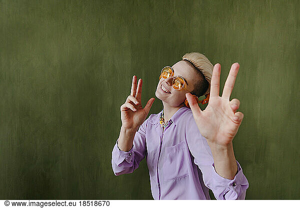 Happy young woman showing peace sign in front of wall