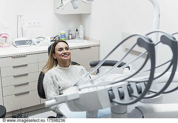 Happy young woman sitting on dentist chair at clinic