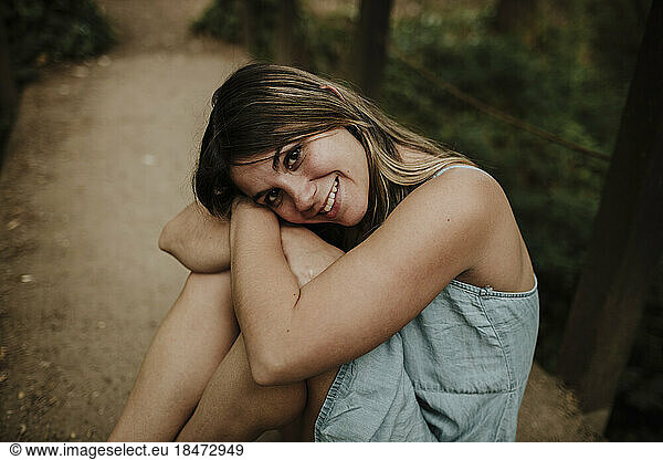 Happy young woman sitting on footpath in forest
