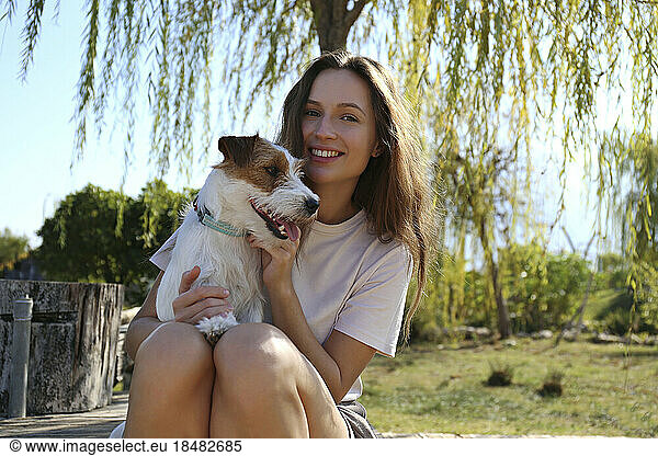 Happy young woman sitting with cute dog at park