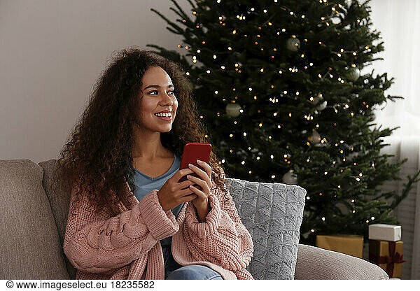 Happy young woman sitting with smart phone at home
