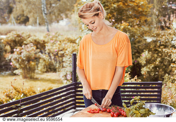 Happy young woman slicing tomatoes on cutting board at yard